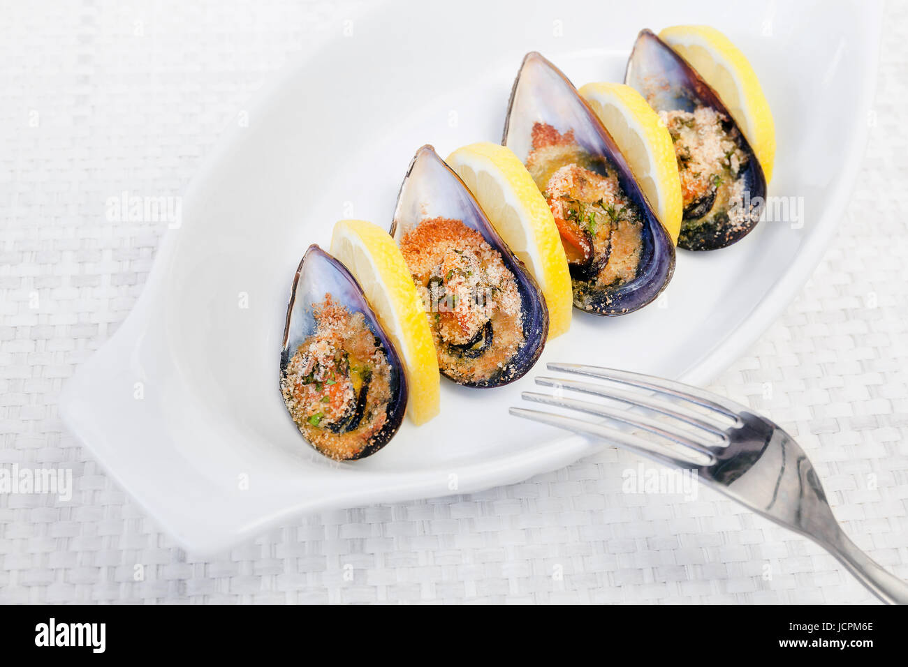 Gegrillte Muscheln gekocht im Ofen, begleitet von Scheiben Zitrone, geriebene Pfanne und Petersilie. Muscheln auf weißen Teller gekocht. Stockfoto