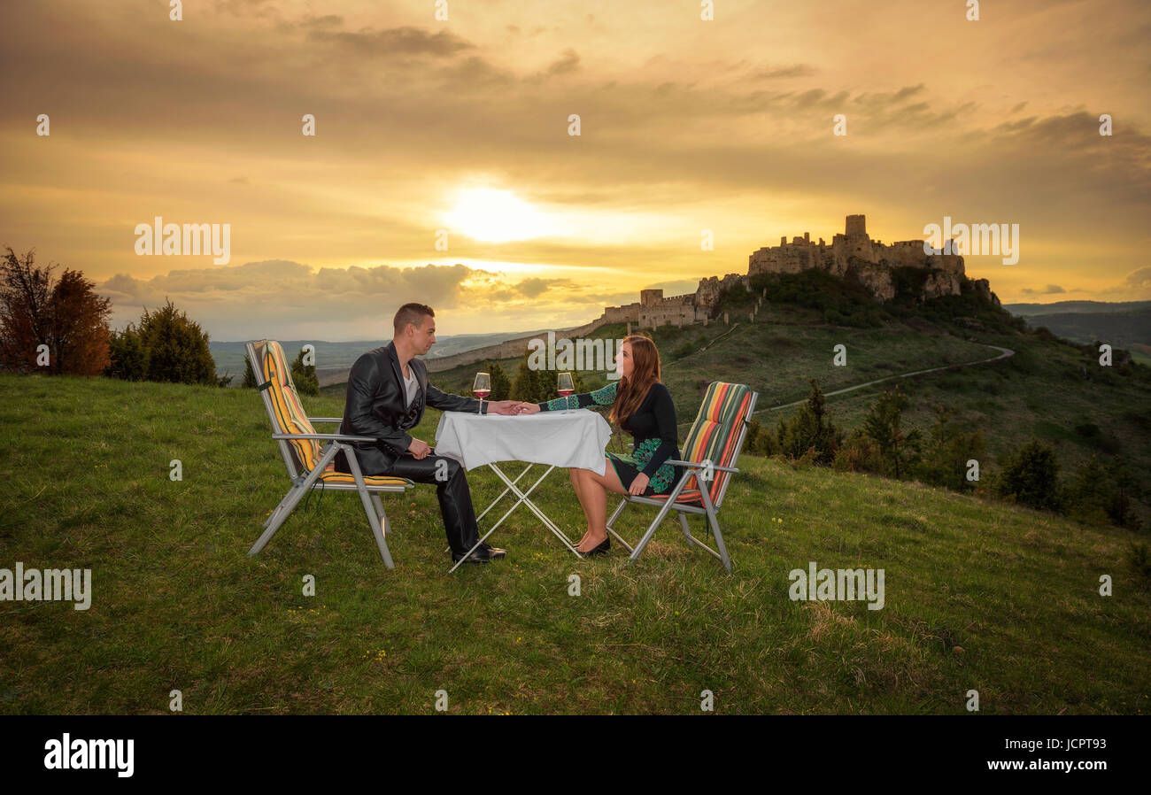 Paar in Liebe trinken roten Wein in der Natur unter den Ruinen einer Burg bei Sonnenuntergang. Stockfoto