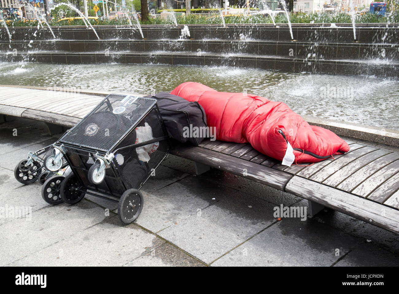 Obdachloser schlafen rau auf Parkbank neben Brunnen am Columbus Circle New York City USA Stockfoto