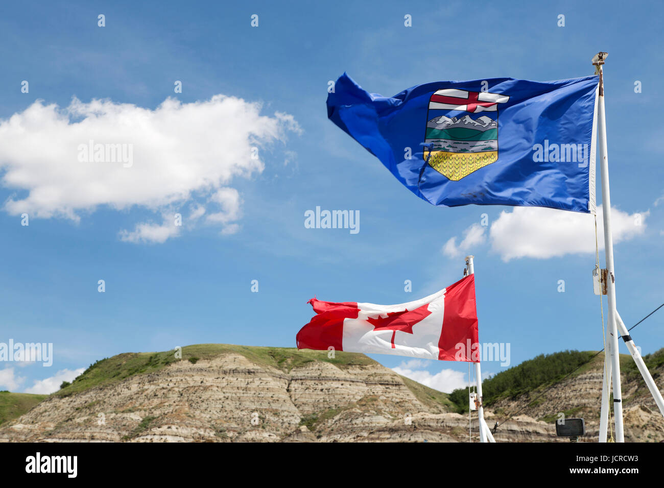Die Alberta und Kanada Fahnen flattern im Wind an der Badlands von Alberta, in der Nähe von Drumheller, in Kanada. Ein Hügel mit freiliegenden, geschichteten Felsen, steht Stockfoto