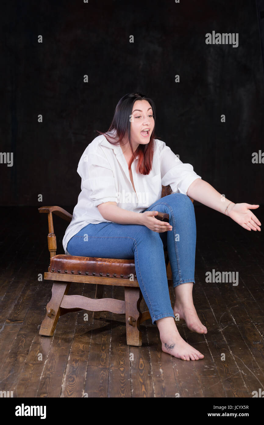 Schöne weiße braune kurzhaarige Hündin mit farbigen in roten enden tragen Männer weißes Hemd und blaue Jeans, sitzt auf einem Vintage Stuhl auf einem dunklen Hintergrund Stockfoto