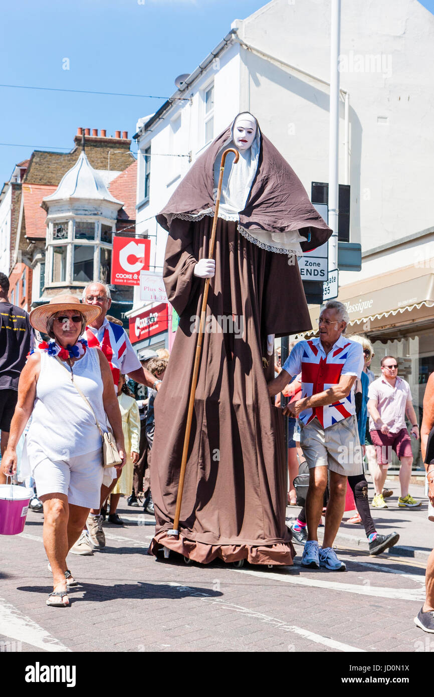 England, Broadstairs. Dickens Festival Woche, die wichtigsten Parade auf  Broadstairs High Street mit verschiedenen Gruppen im Viktorianischen Kostüm.  Zwei Männer in Union Jack t-Shirts tragen eine 12 Fuß hohe bildnis einer  Nonne'