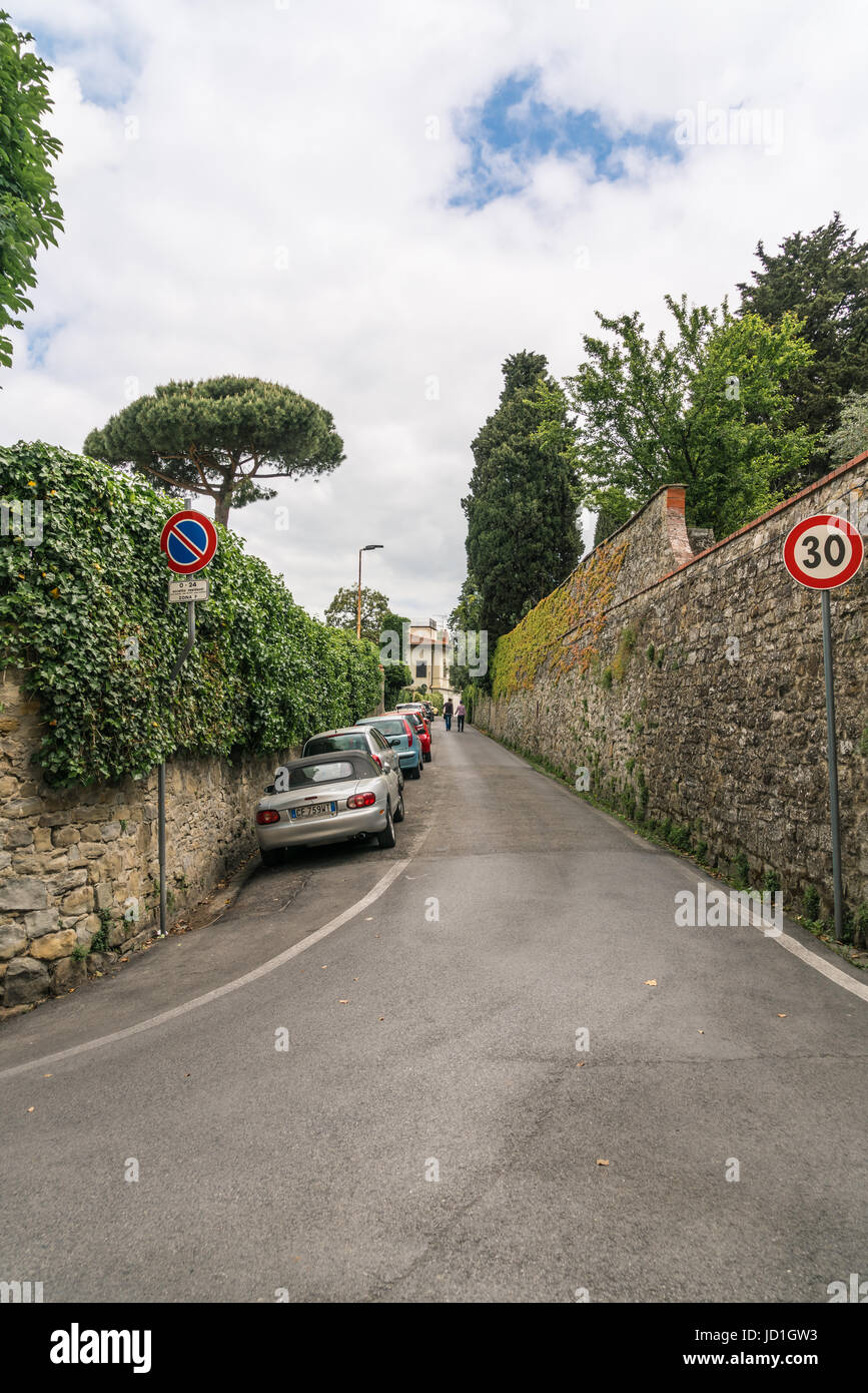 Bergauf Gasse mit Autos auf der einen Seite und einer Steinmauer andererseits in Fiesole, Italien Stockfoto