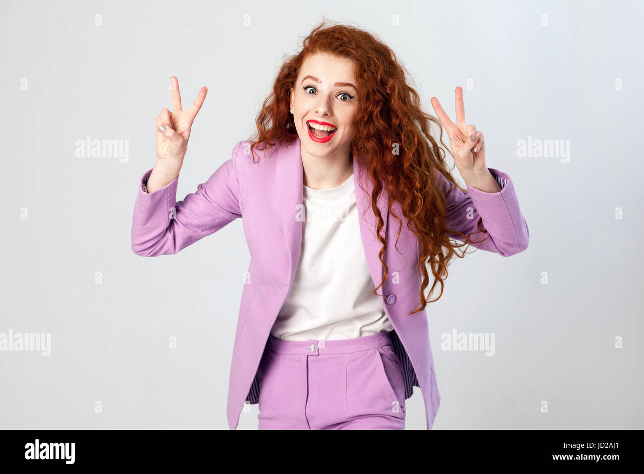 Porträt der erfolgreiche glücklich schöne Geschäftsfrau mit rot - braune Haare und Make-up in rosa Anzug mit V-Zeichen oder Frieden. Blick in die Kamera mit Stockfoto