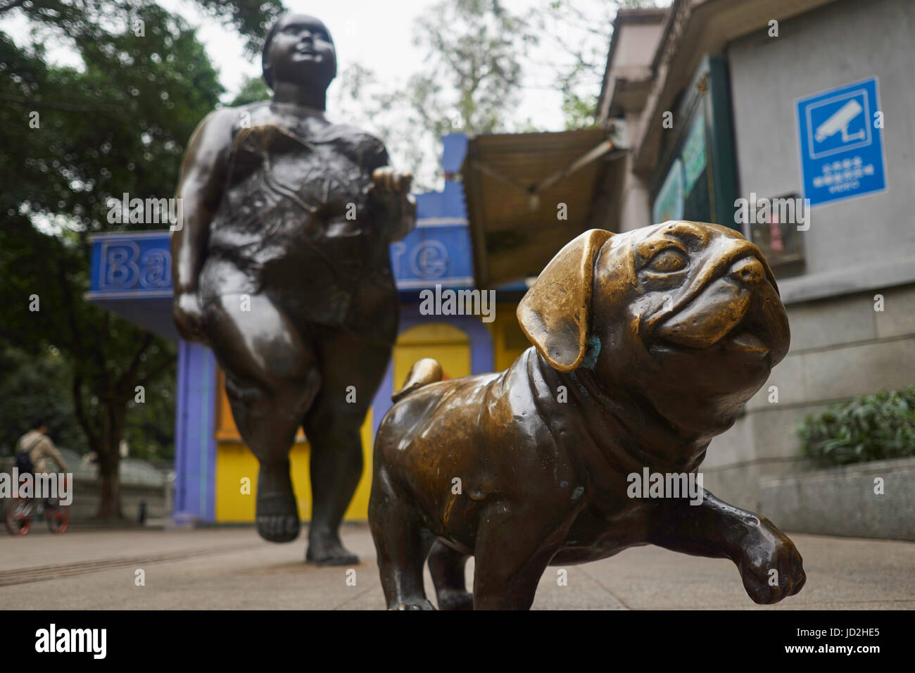 Bronze-Skulptur einer Frau zu Fuß einen chinesische Mops Hund an der Leine - Streetart auf Shamian Island, Guangzhou, China Stockfoto