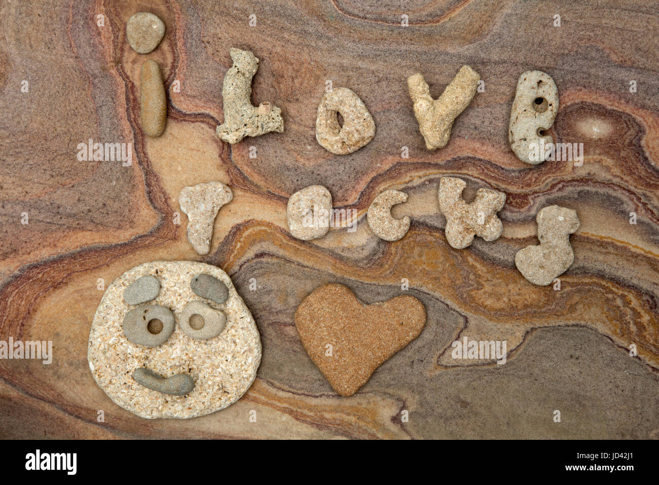 "Ich liebe Felsen', ausgeschrieben in den natürlichen Felsen aus Florida, mit Naturstein lustiges Gesicht und Herz, auf Sandstein Hintergrund aus Indien Stockfoto