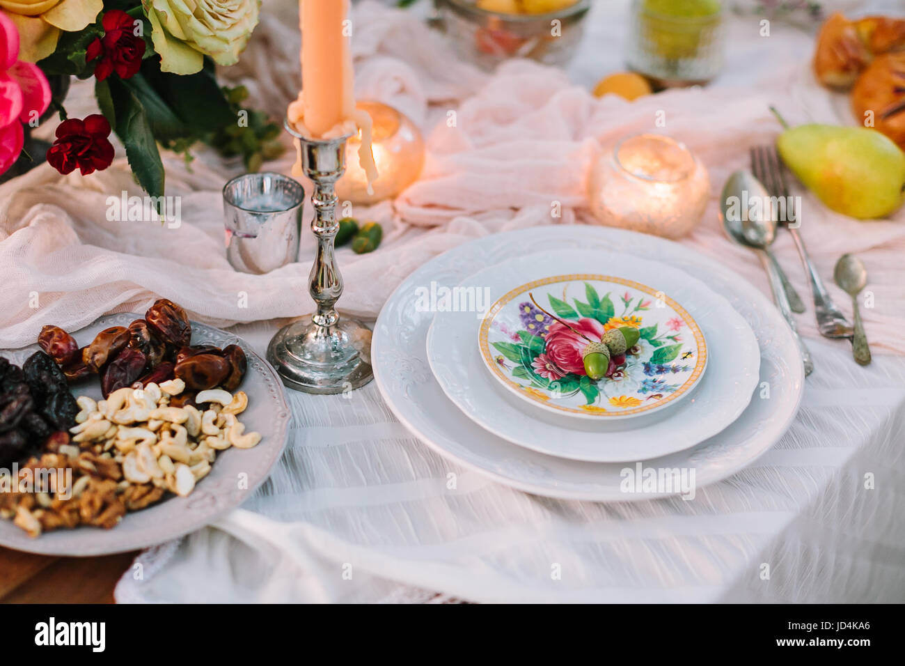 Hochzeit, Dekoration, Einstellung, Vegetarismus, Lifestyle-Konzept - Stillleben von Table linens mit schneeweißen drapieren, Platten mit Blumendruck, Kerzen, Tafelsilber, Haufen von Blumen und Nüssen Stockfoto