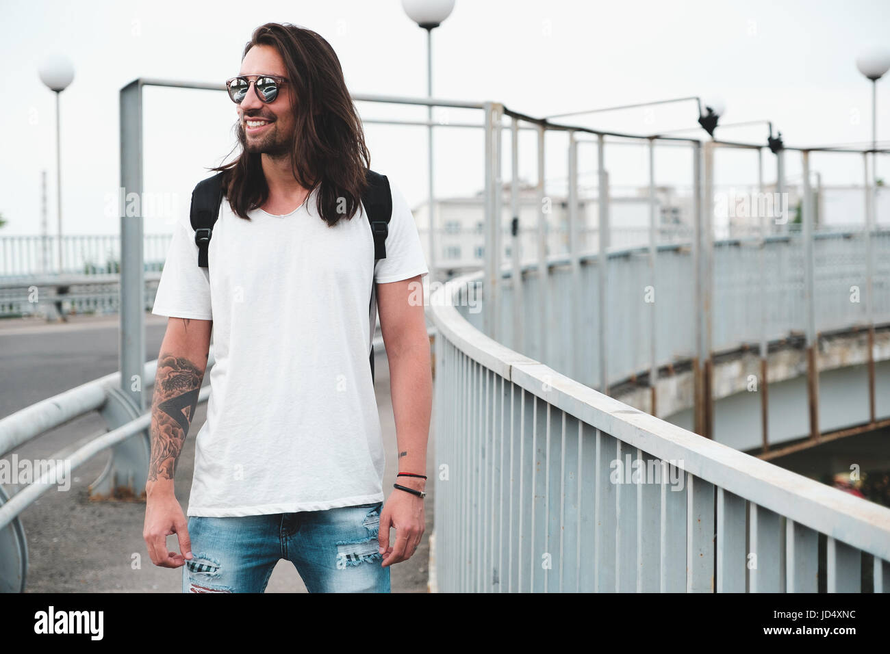 Stilvolle Hipster-Modell mit langen Haaren Lebensstil auf der Straße. Gekleidet in ein weißes T-shirt und zerrissene Bluejeans in der Stadt Stockfoto