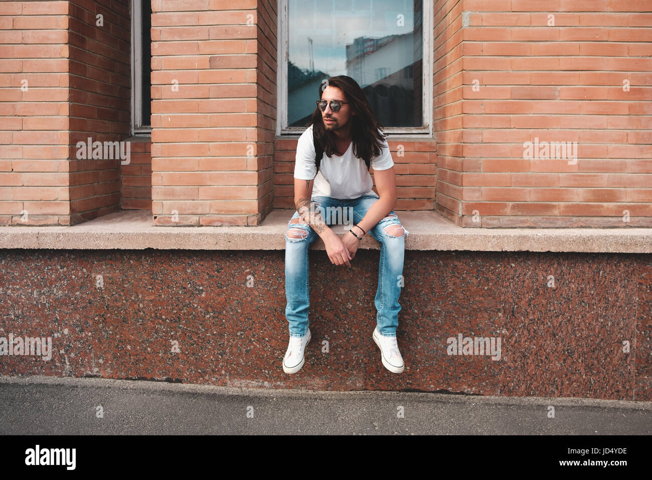 Stilvolle Hipster-Modell mit langen Haaren Lebensstil auf der Straße. Gekleidet in ein weißes T-shirt und zerrissene Bluejeans in der Stadt Stockfoto