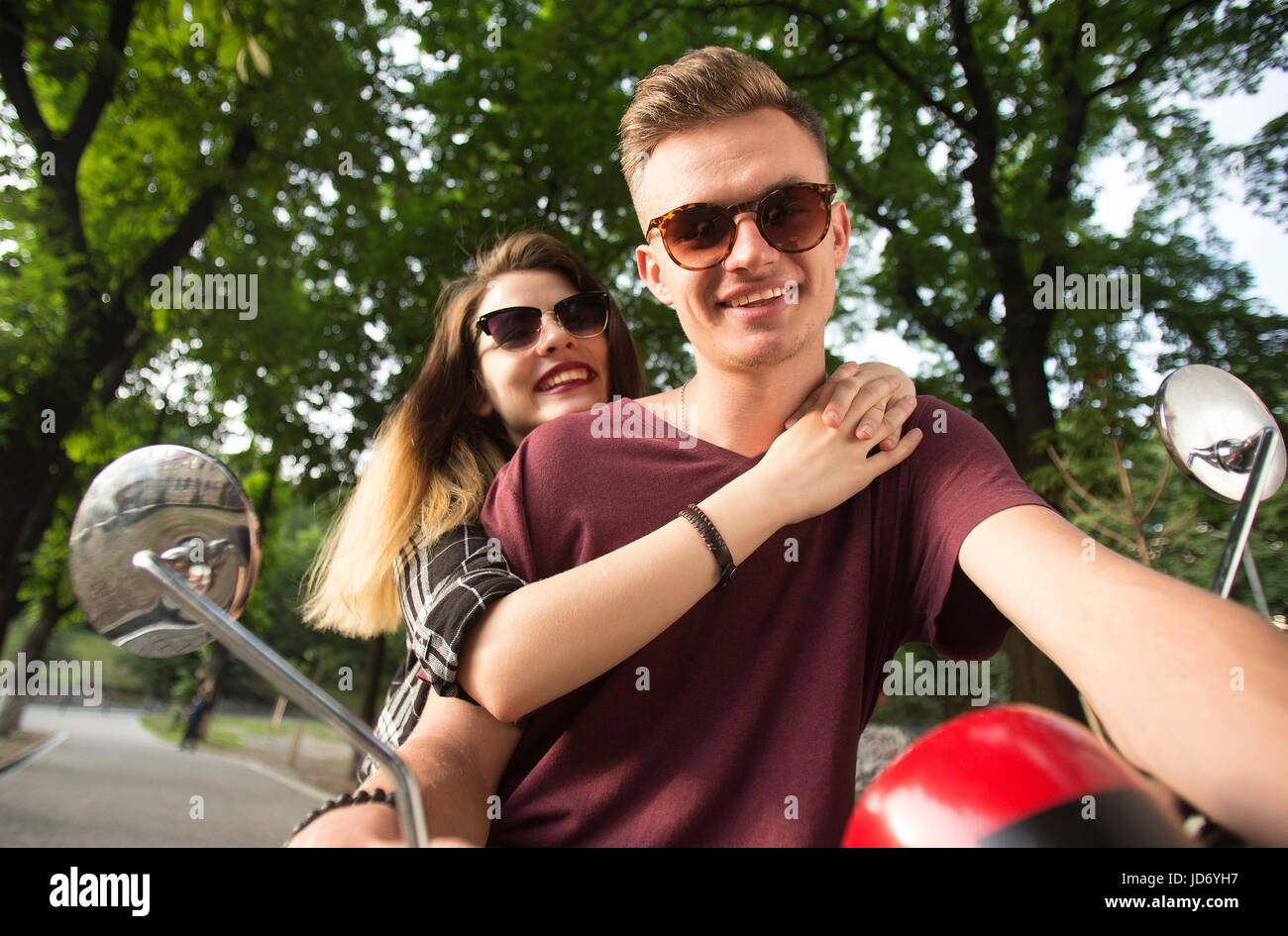 Junges attraktives paar Teenager trägt Sonnenbrille auf Retro-Motorrad im Park, Hipster-Konzept, 120FPS slowmotion Stockfoto