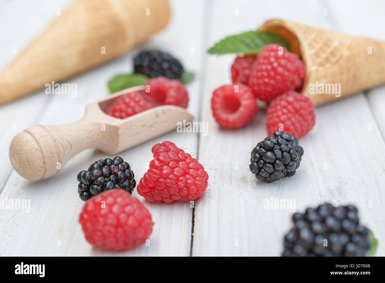 Kegel und Löffel mit Himbeeren, Brombeeren und einem Zweig Minze Ausbreitung über eine weiße Tischplatte Stockfoto