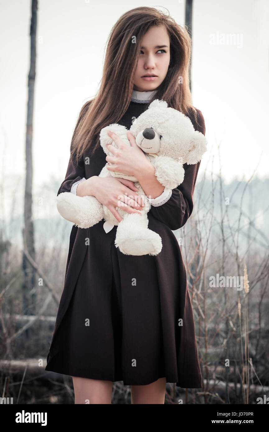 schöne Teenager-Mädchen mit Teddybär Spielzeug in die Hände auf den Hintergrund des verbrannten Waldes Stockfoto