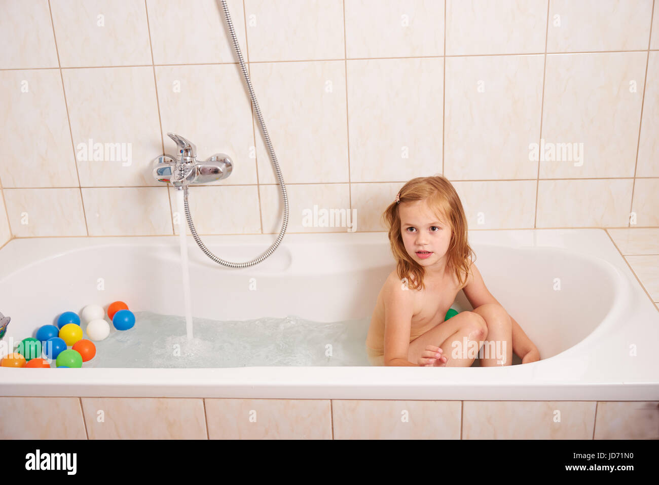 Ein kleines Mädchen in eine Badewanne mit farbigen Kugeln spielen Stockfoto