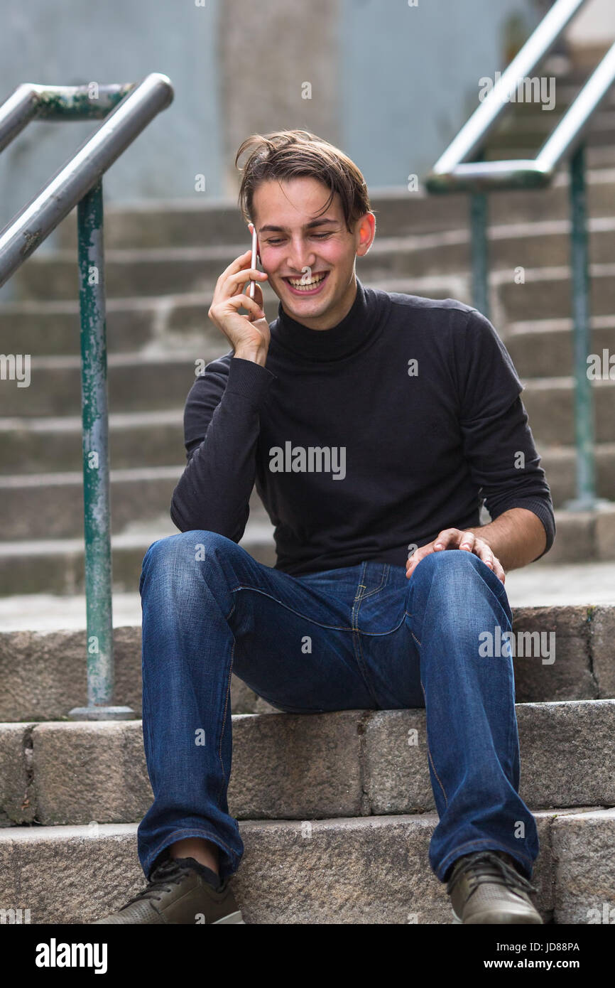 Junger Mann sitzend auf Außentreppen am Handy sprechen. Stockfoto
