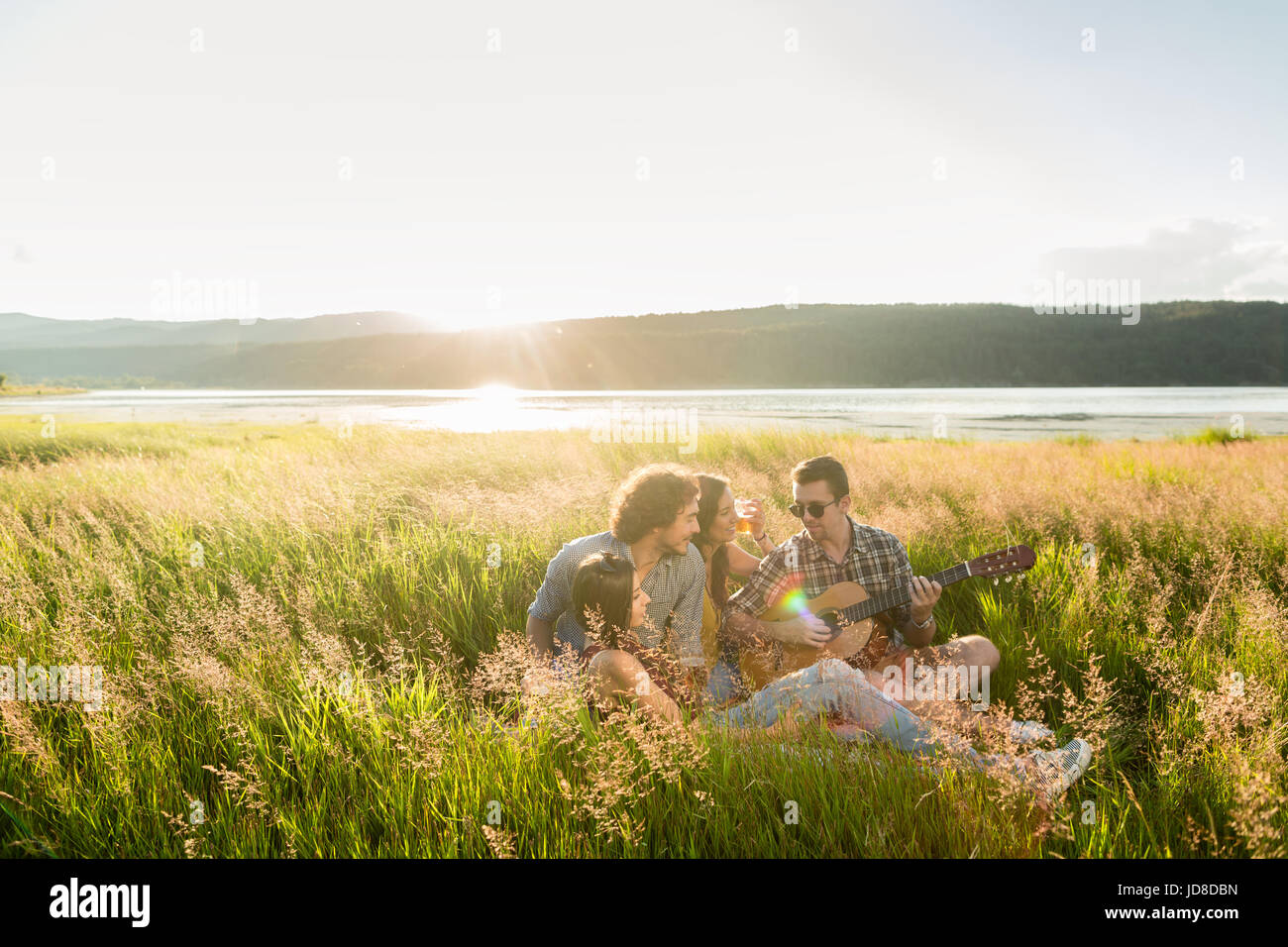 Gruppe von Freunden in Landschaft bei Sonnenuntergang spielen Gitarrenmusik Stockfoto