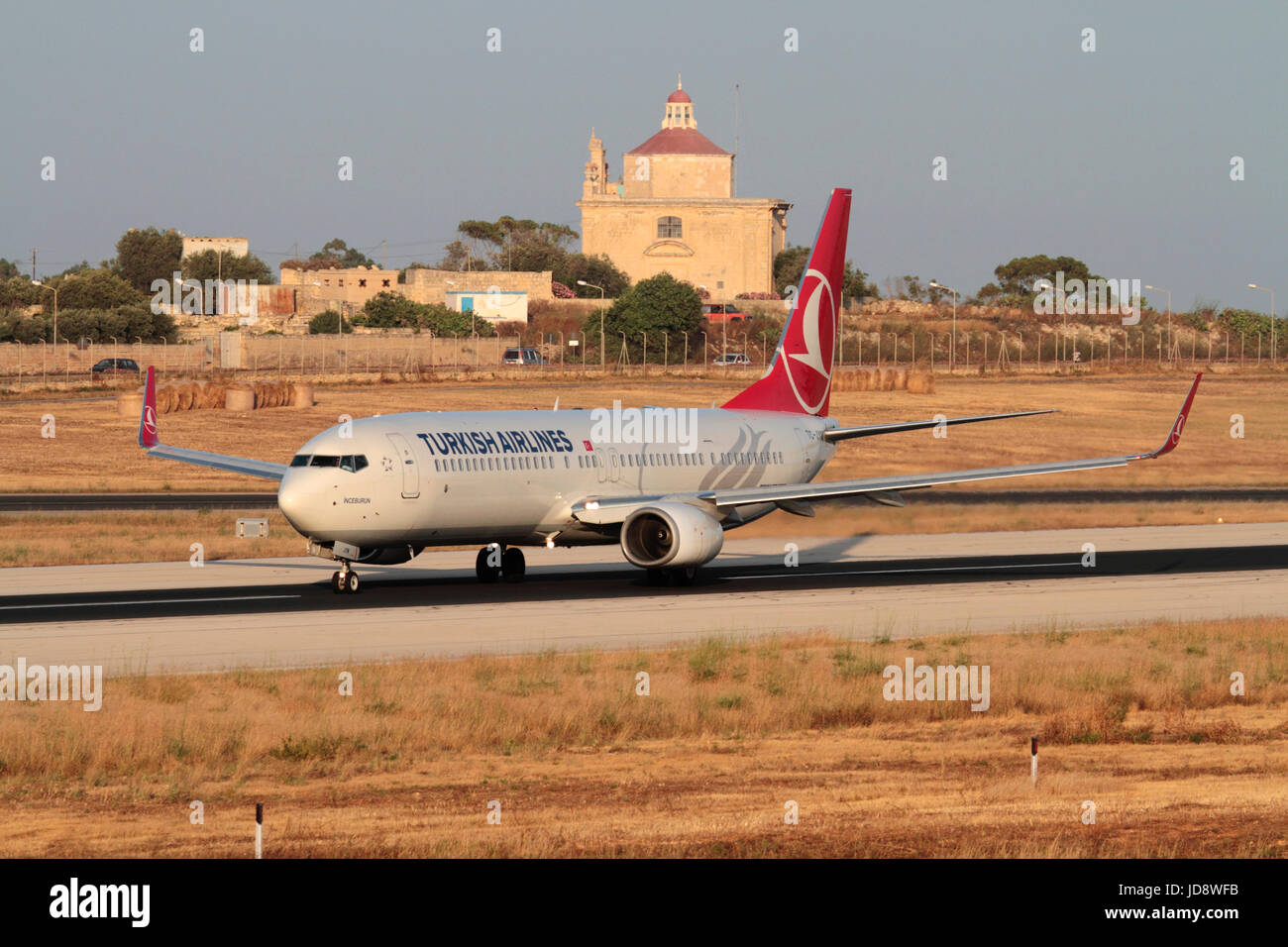 Turkish Airlines Boeing 737-900ER Passagierjet auf der Start- und Landebahn am Flughafen Malta, mit Ta' Loretu Chapel, Gudja, im Hintergrund. Gewerblicher Flug. Stockfoto
