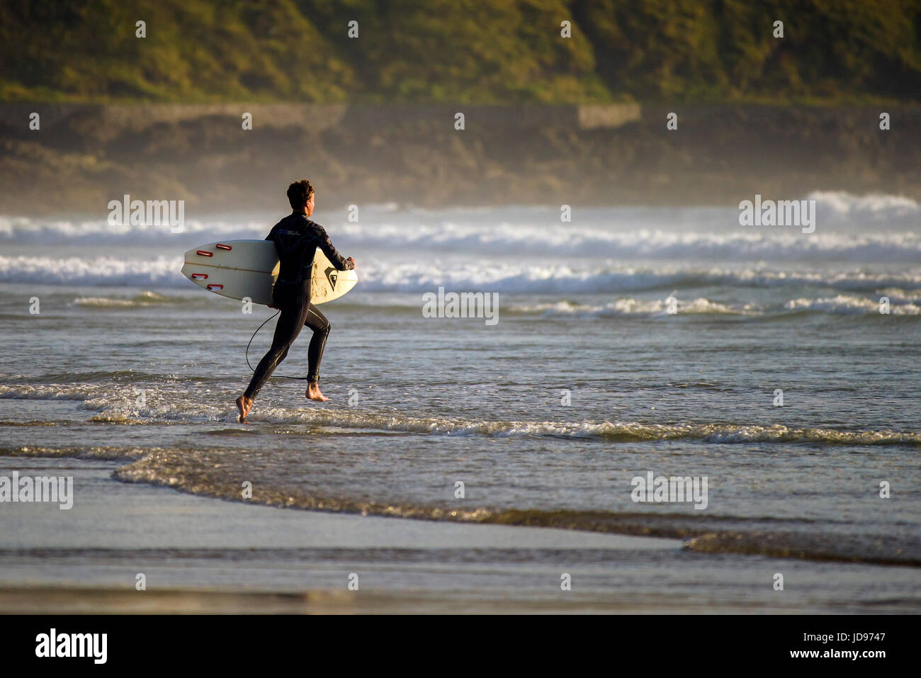 Ein Surfer, der am Fistral Beach, Newquay, Cornwall ins Meer läuft. Stockfoto