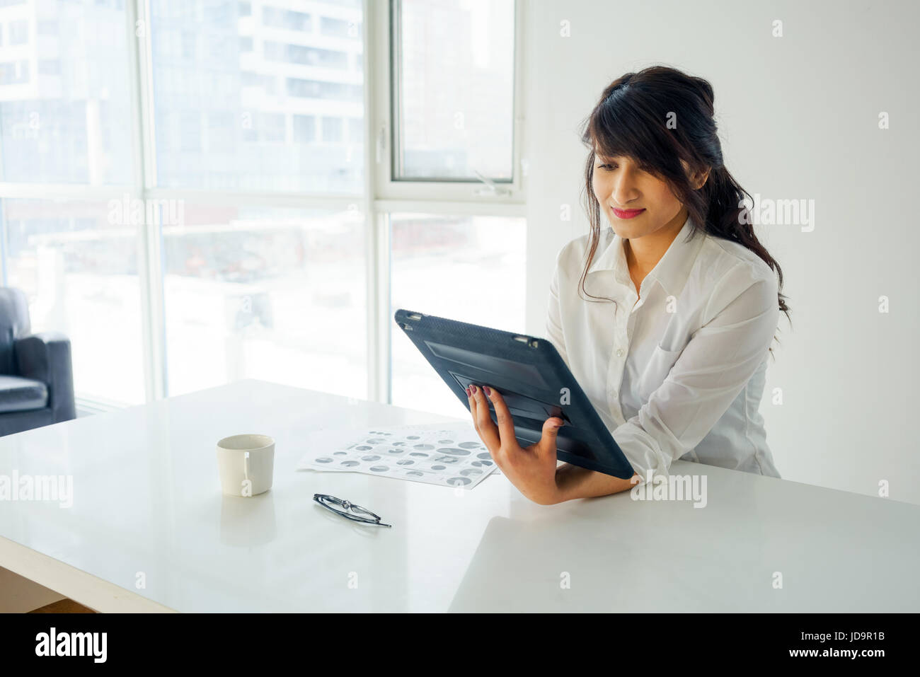 Junge Frau mit digital-Tablette am Schreibtisch, im Innenbereich durch Fenster. junge Erwachsene arabischen hübsche 20 Jahre alt Stockfoto