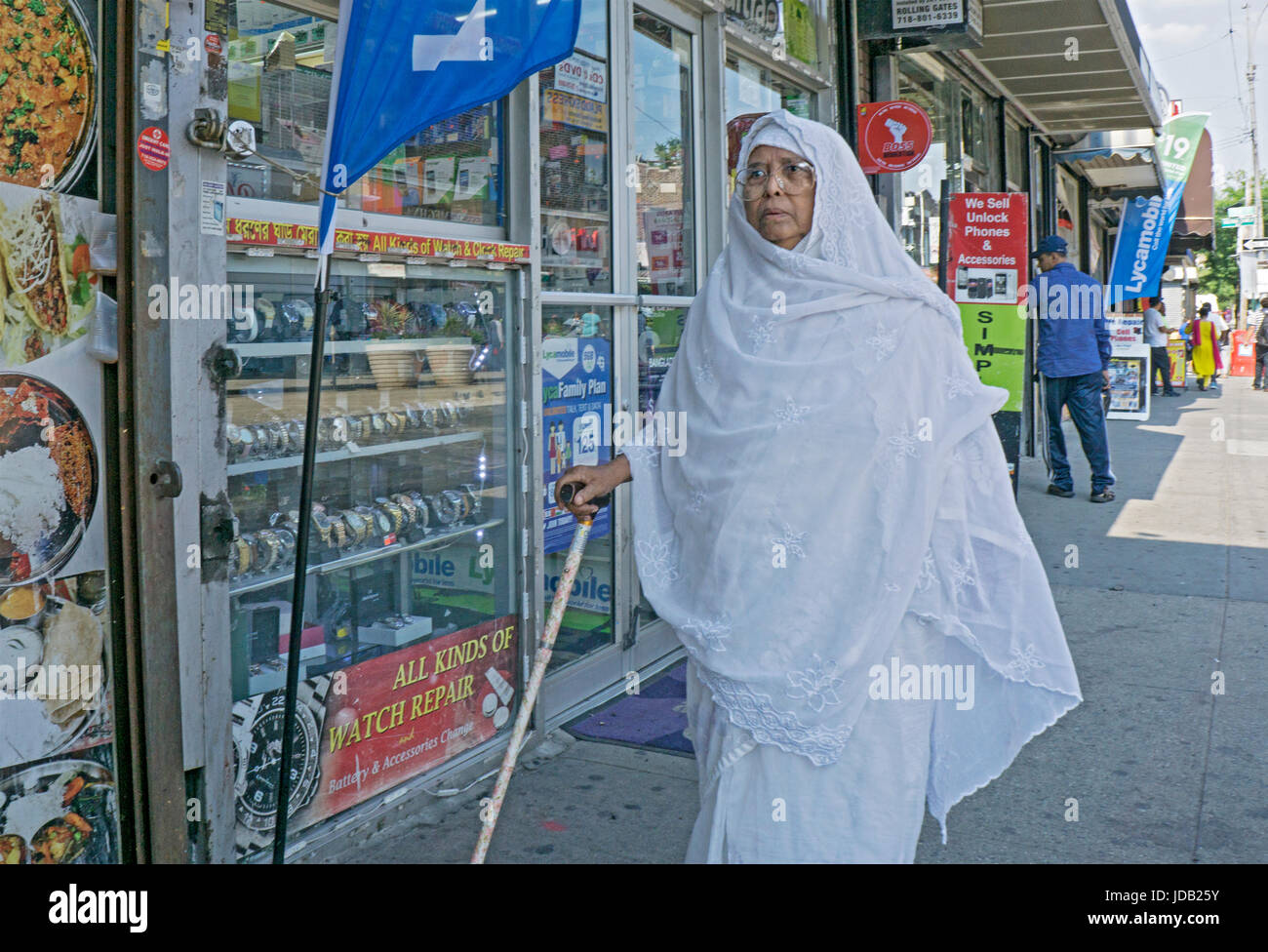 Eine ältere muslimische Frau in traditioneller Kleidung auf der Straße mit Hilfe von einem Stock. In Jackson Heights in Queens, New York City. Stockfoto