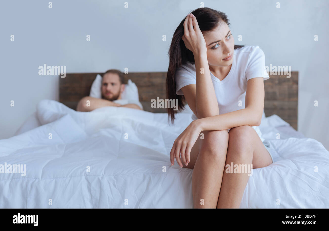 Verärgert Frau sitzt am Bett mit wütenden Mann hinter Stockfoto