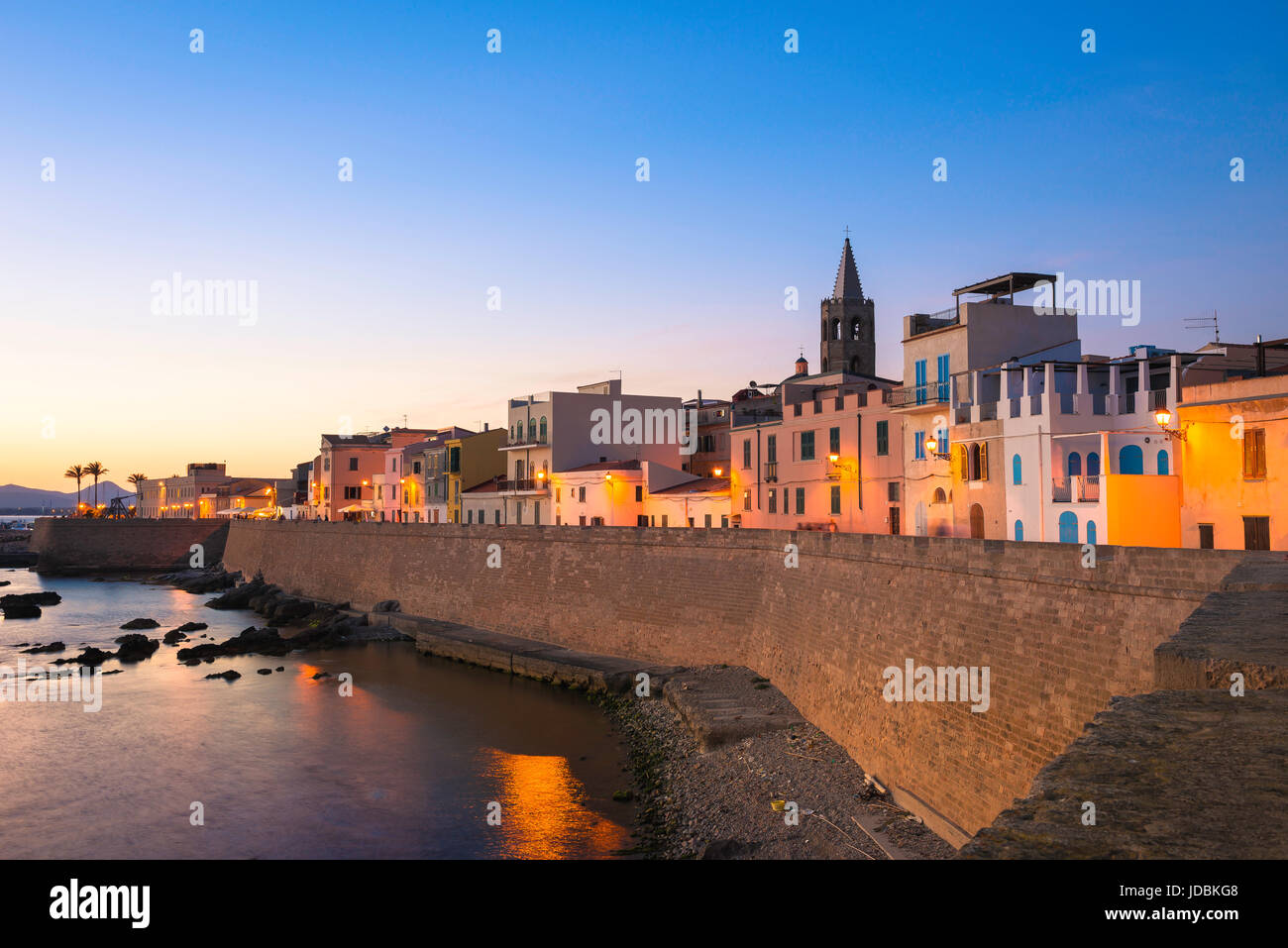 Alghero Stadtbild Dämmerung, einen Blick auf die Skyline der alten Stadt in Alghero an einem Sommerabend mit der großen mittelalterlichen Ufermauer im Vordergrund, Sardinien. Stockfoto