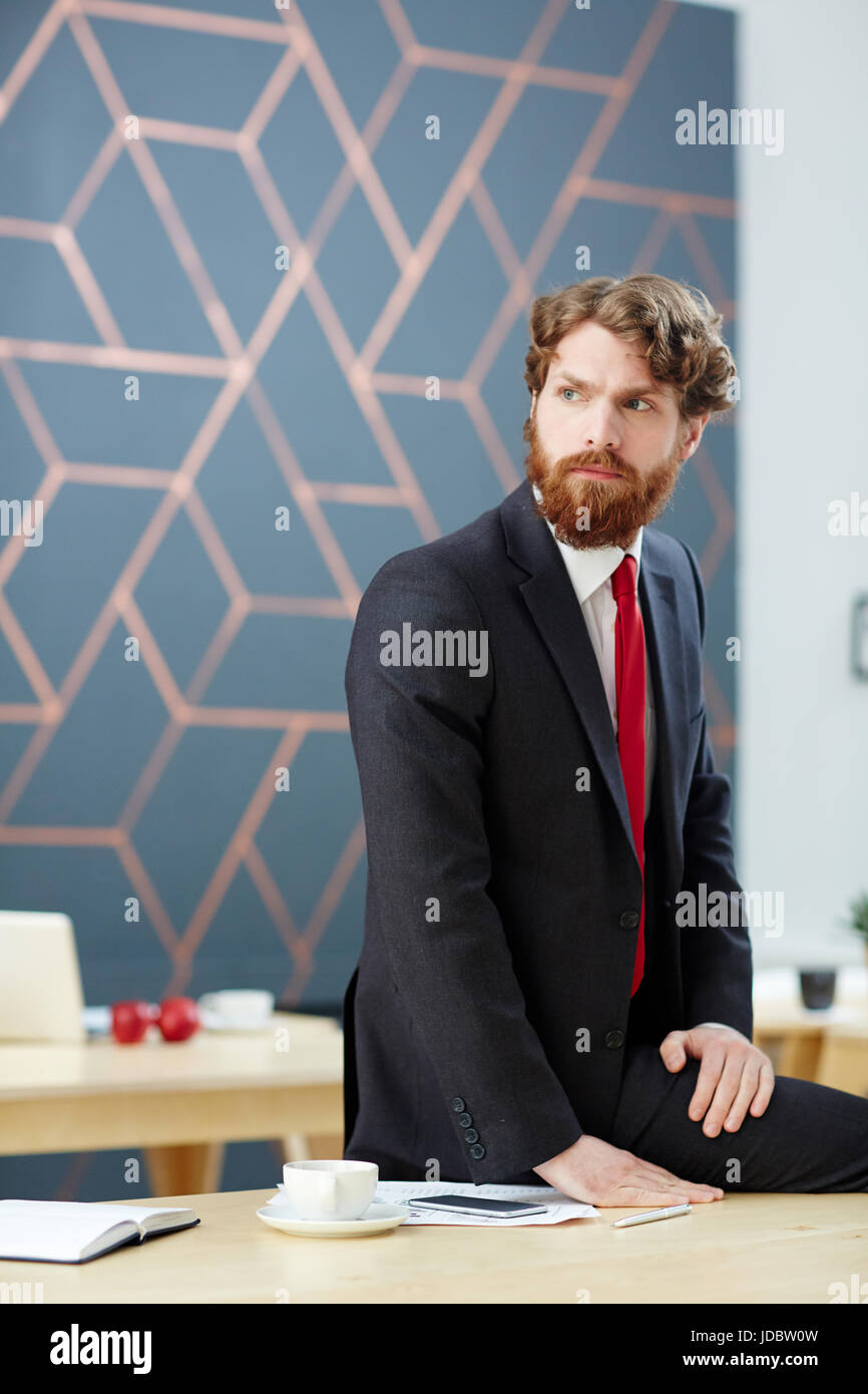 Ernsthafte bärtiger Mann in Anzug Standortwahl auf Schreibtisch Stockfoto