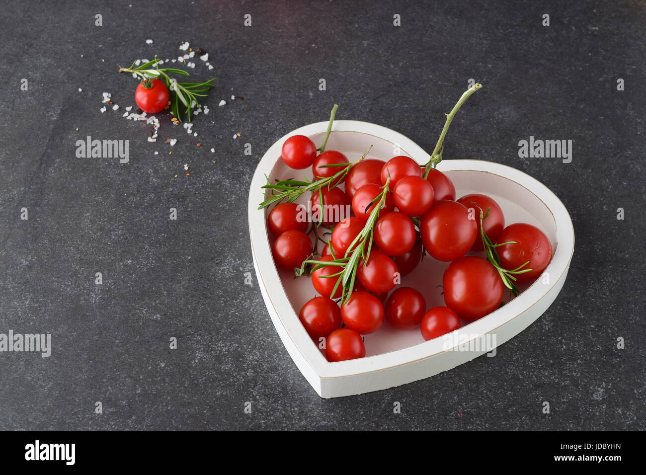 Verschiedene Arten von Tomaten auf Zweigen im Herzen geformt Tablett auf einem dunklen grau abstrakten Hintergrund. Platz für Text. Gesunde Ernährung-Konzept Stockfoto