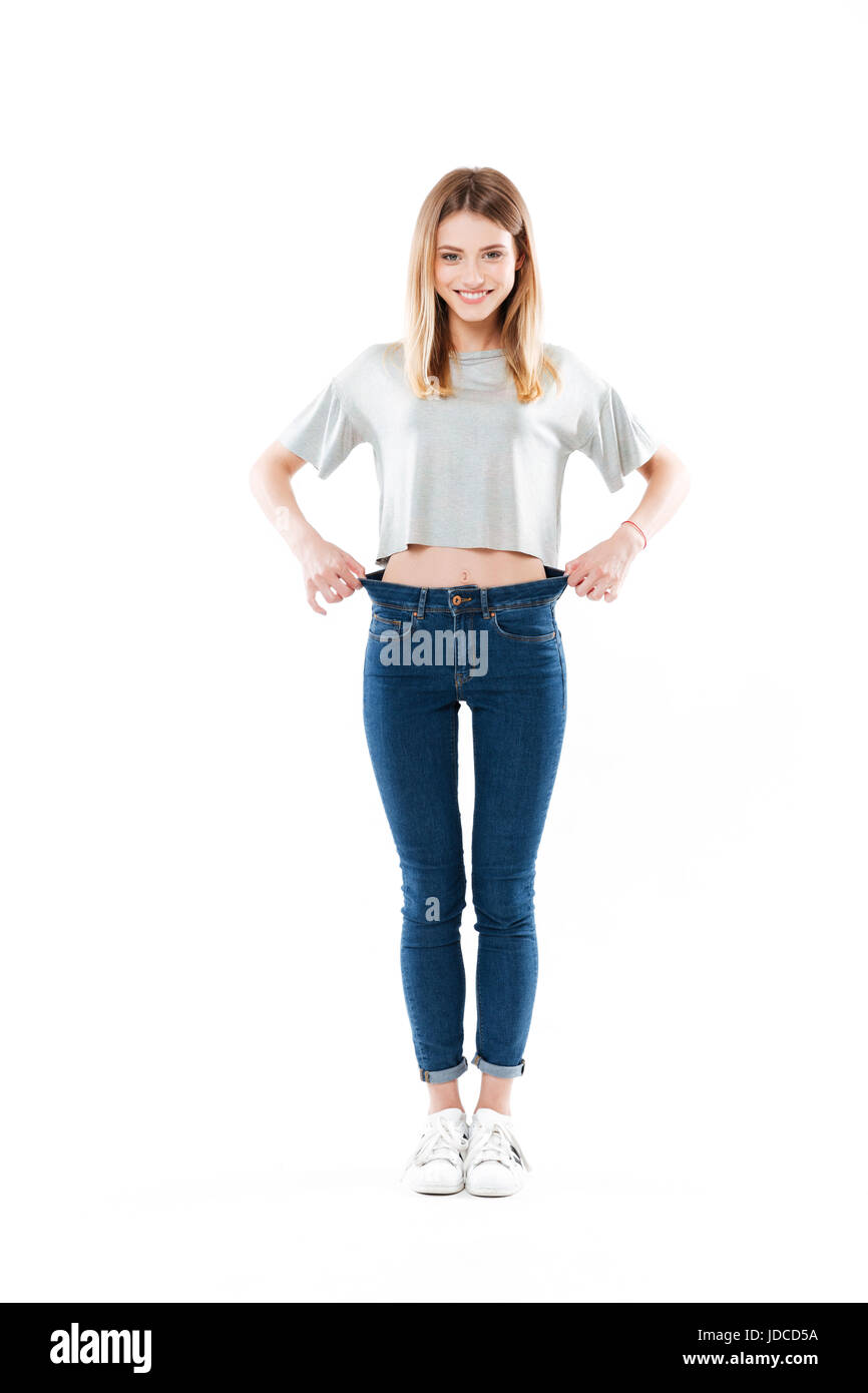 In voller Länge Portrait von ein fröhliches zufrieden Mädchen stehen und zeigen ihre Gewichtsverlust isoliert auf weißem Hintergrund Stockfoto