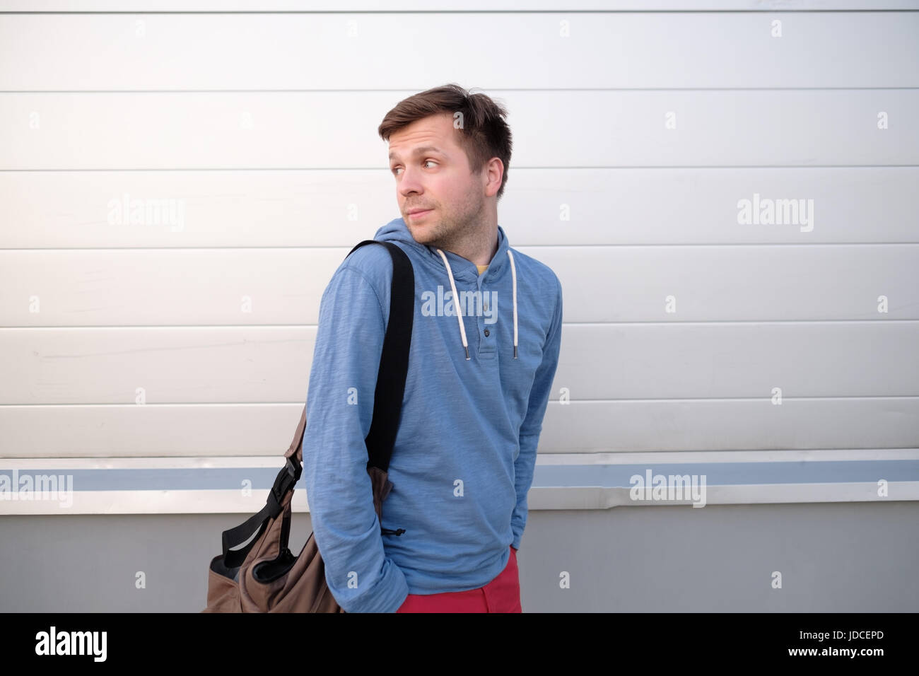 Hübscher junger Mann in eine urbane Mode Lifestyle Kleidung zu Fuß und auf der Suche zurück. Stockfoto