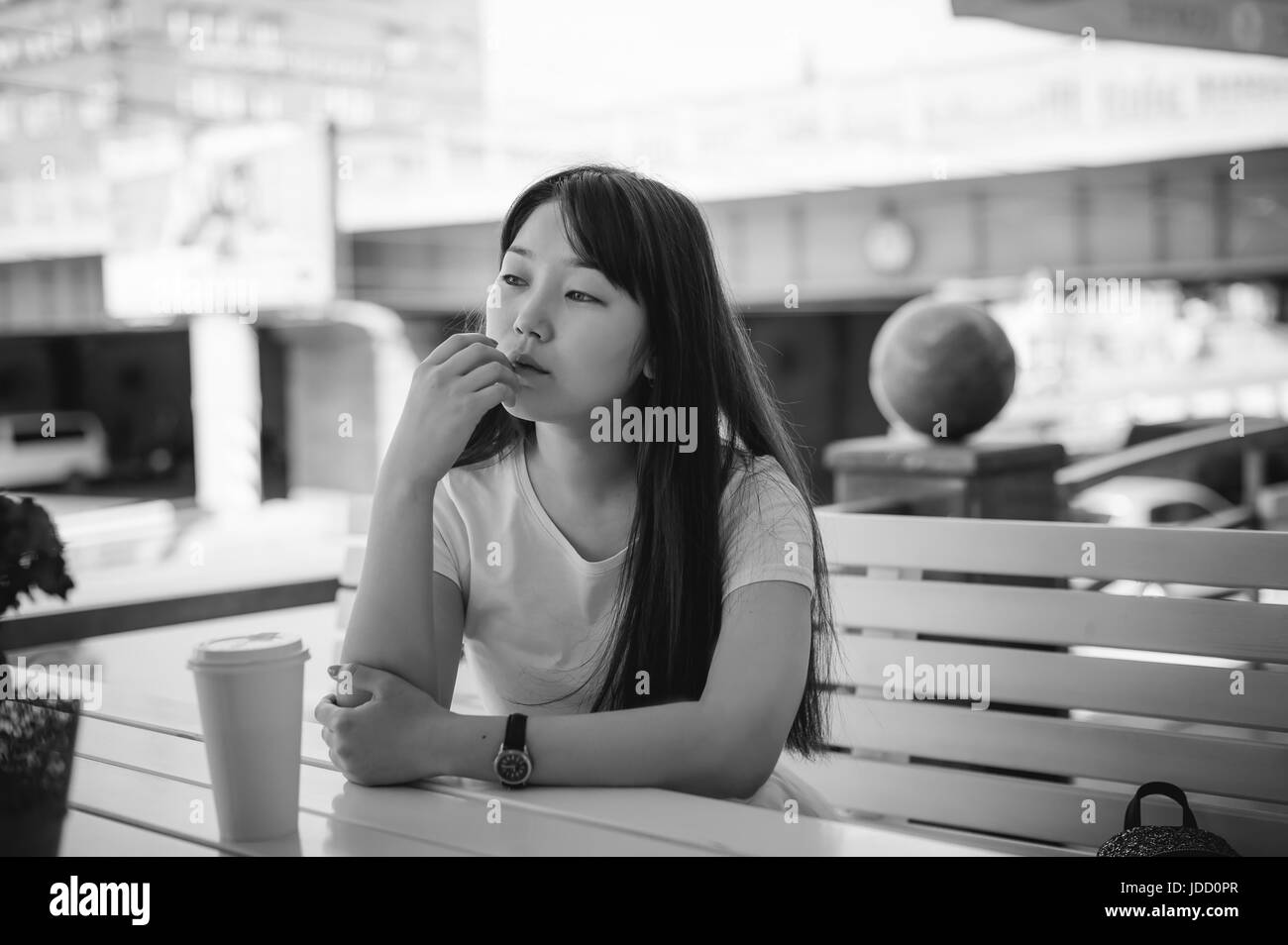 Süße junge Asiatin im Café im Freien. Mädchen im weißen T-shirt, mit langen Haaren in einfachen hellen gemütlichen Innenraum Restaurant Urban Style, lerne Stockfoto