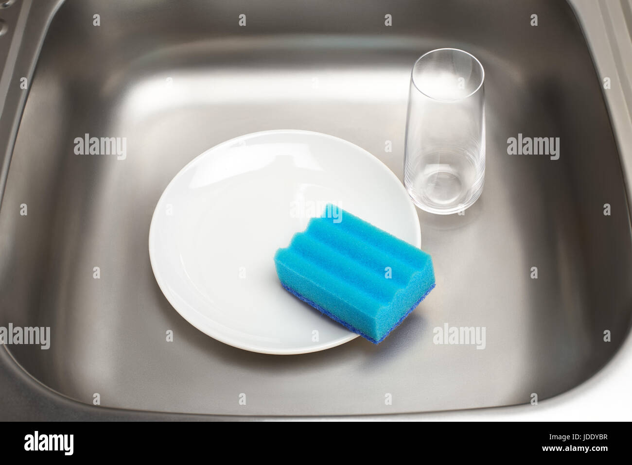 Nahaufnahme der Küchenspüle mit sauberen weißen Teller, blauen Reinigungsschwamm und Trinkglas Stockfoto