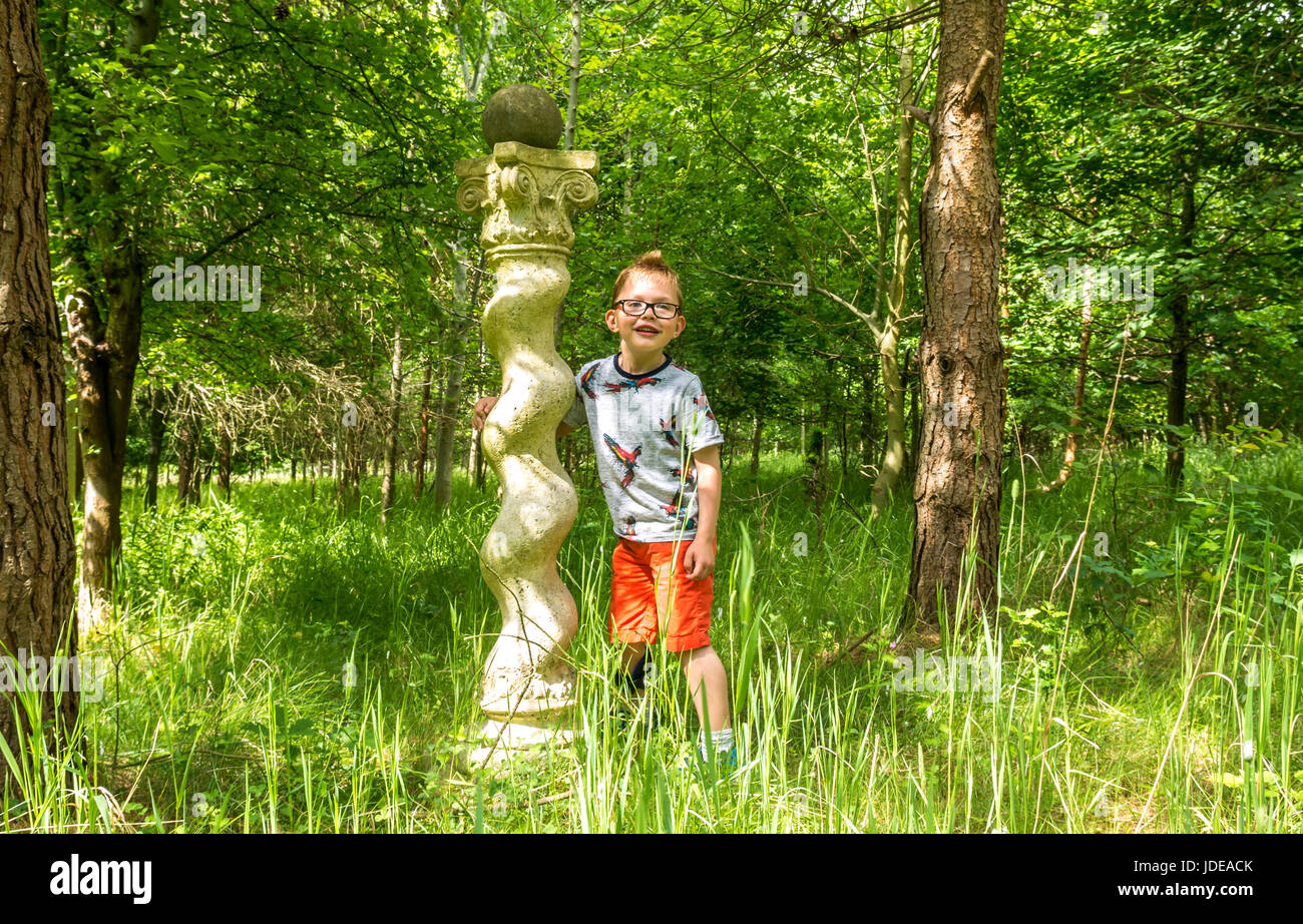 Eine Skulptur in einem grasbewachsenen Wald mit einem kleinen Jungen mit Brille in einem T-Shirt und Shorts an einem Sommertag, Schottland, Großbritannien Stockfoto
