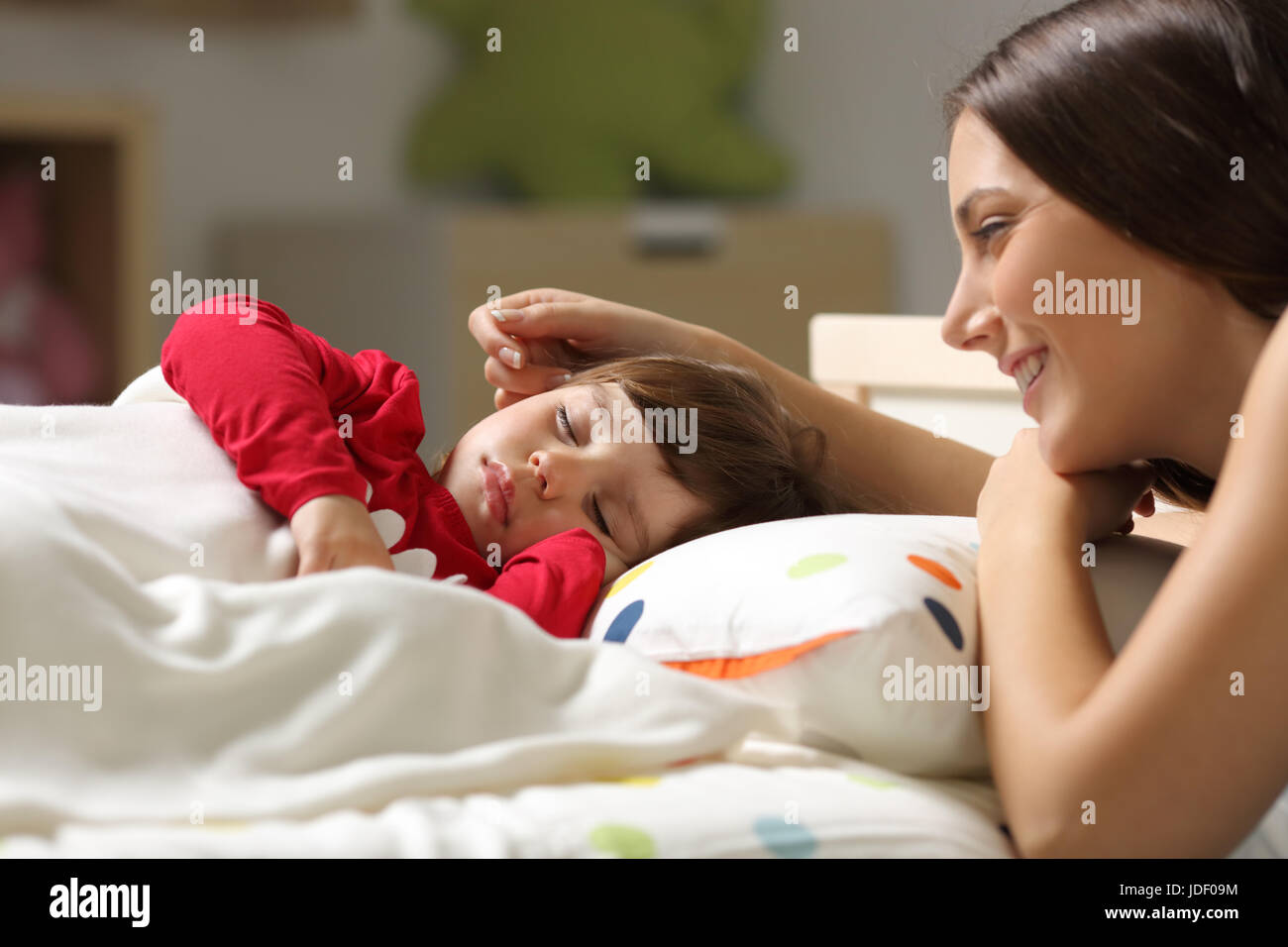 Stolze Mutter, die gerade auf dem Bett, um ihre Tochter in einem Schlafzimmer zu Hause schlafen Stockfoto