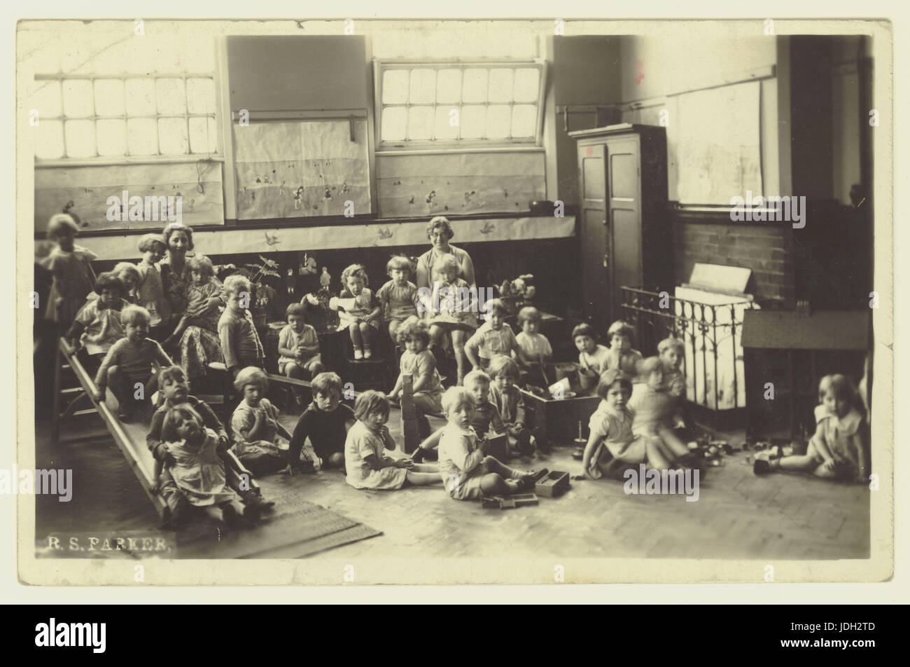 1920er Jahre Postkarte von St. Andrews Schule, Homer Street, Manchester - Säuglinge oder Kindergarten-Kinder in der Halle mit Spielgeräten, UK Stockfoto