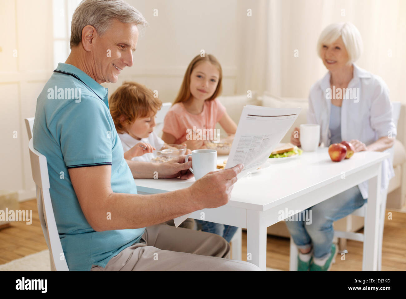 Positiven smart Großvater liest eine Zeitung beim Frühstück Stockfoto