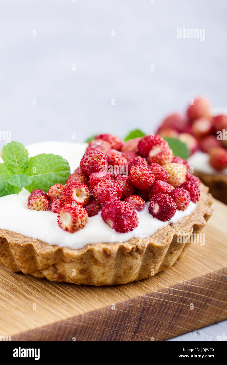 Wilde Erdbeeren Törtchen mit Creme füllen, köstliche Sommer Mini Obstkuchen auf rustikalen Schneidebrett Stockfoto