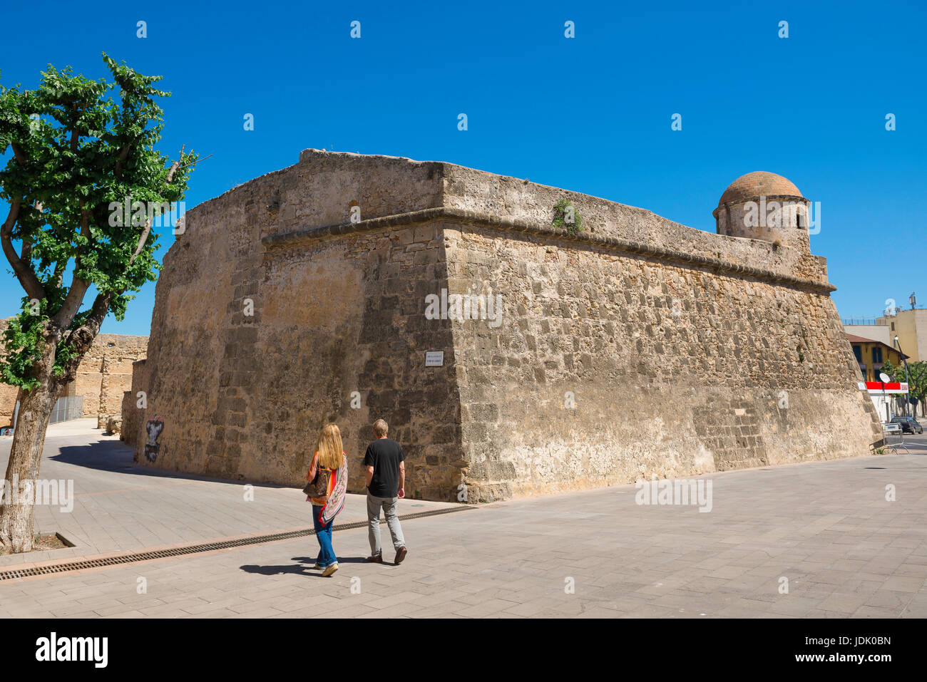 Gehen Sie Alghero Sardinien, ein paar Touristen vorbei an einem Abschnitt der Stadtmauer bekannt als der Bastione La Maddalena in der Altstadt von Alghero, Sardinien. Stockfoto
