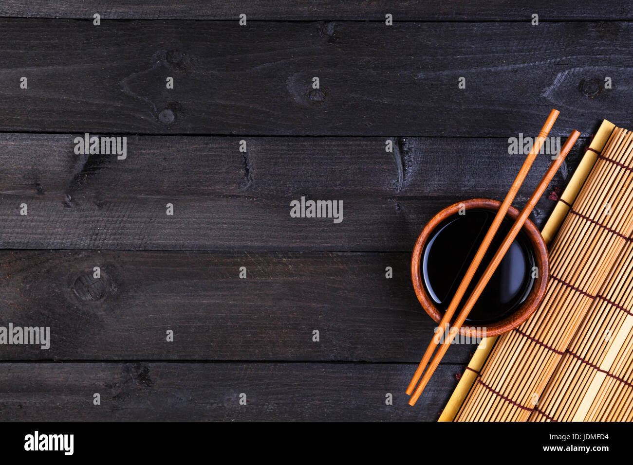 Hintergrund für Sushi. Bambusmatte und Sojasauce auf schwarzer Holztisch. Draufsicht mit Textfreiraum Stockfoto