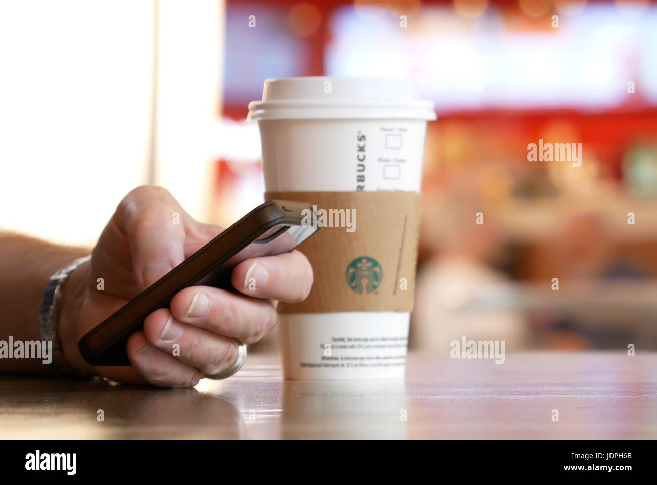 Burnaby, BC, Kanada - 4. Mai 2017: Mann lesen Nachricht auf seinem Handy und trinken Starbucks heißen Getränk Kaffee mit blur Bewegung Menschen am Food-court Stockfoto