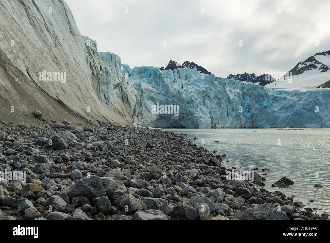 Die blau-weißen Vorderseite eines Gletschers erreicht das Meer über einen Boulder Beach in Spitzbergen Stockfoto