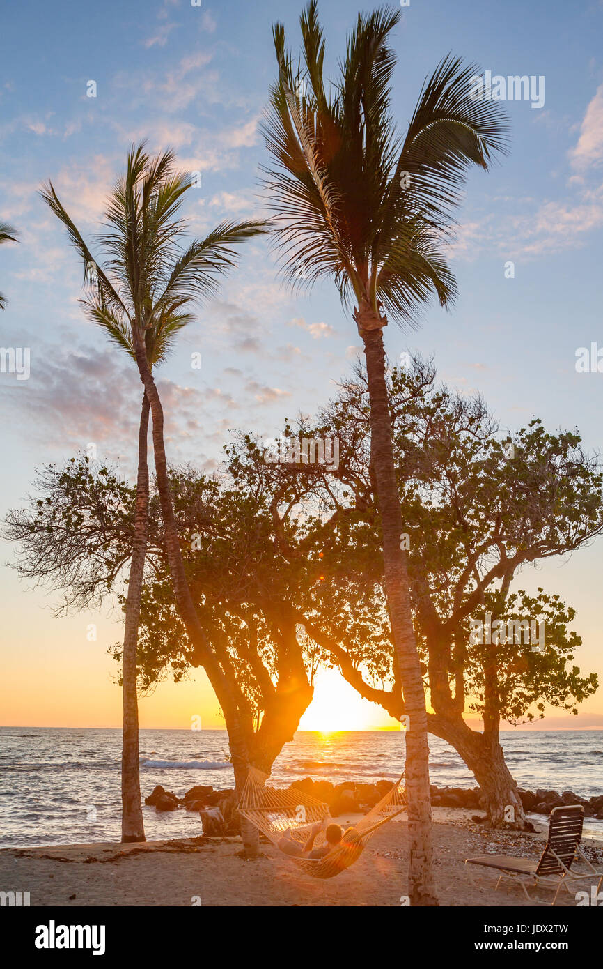 paar zum Entspannen in der Hängematte zwischen zwei Palmen am Strand bei Sonnenuntergang auf Hawaii Stockfoto