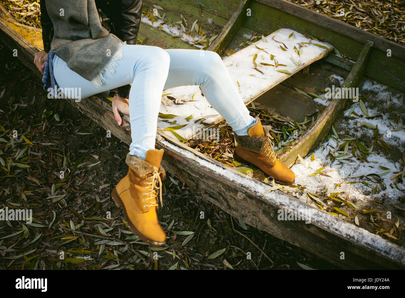 schlanke Mädchen Beine in Blue Jeans und braune Stiefel. Mädchen saß auf  dem umgedrehten Boot auf das Ufer, gelbes Herbstlaub Stockfotografie - Alamy
