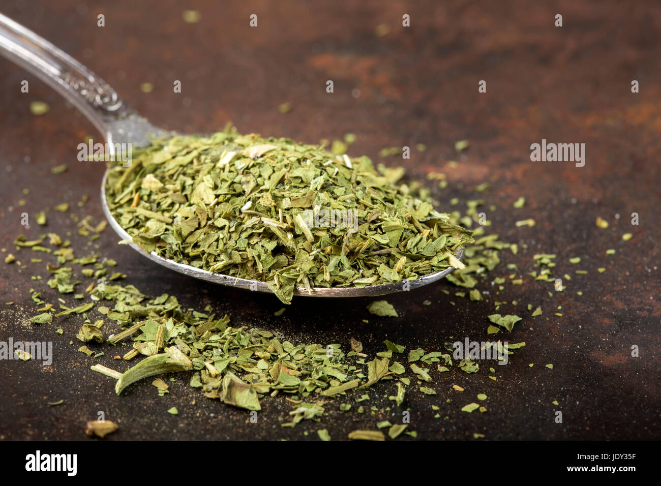 Löffel gefüllt mit getrockneten Liebstöckel auf rostigen Hintergrund Stockfoto