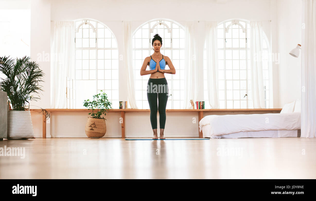 Porträt in voller Länge einer fitten jungen Frau, die mit zuhause verbundenen Händen steht. Fitness-Frau, die drinnen meditiert. Stockfoto