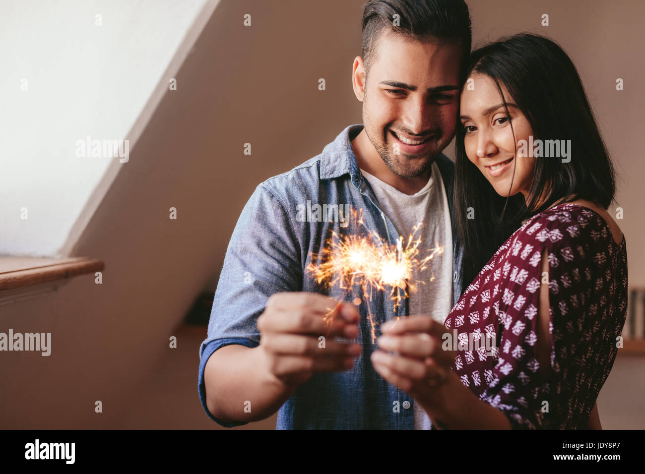 Lächelnder junger Mann und Frau mit Wunderkerzen drinnen. Junges Liebespaar mit Wunderkerzen zu Hause zu feiern. Stockfoto