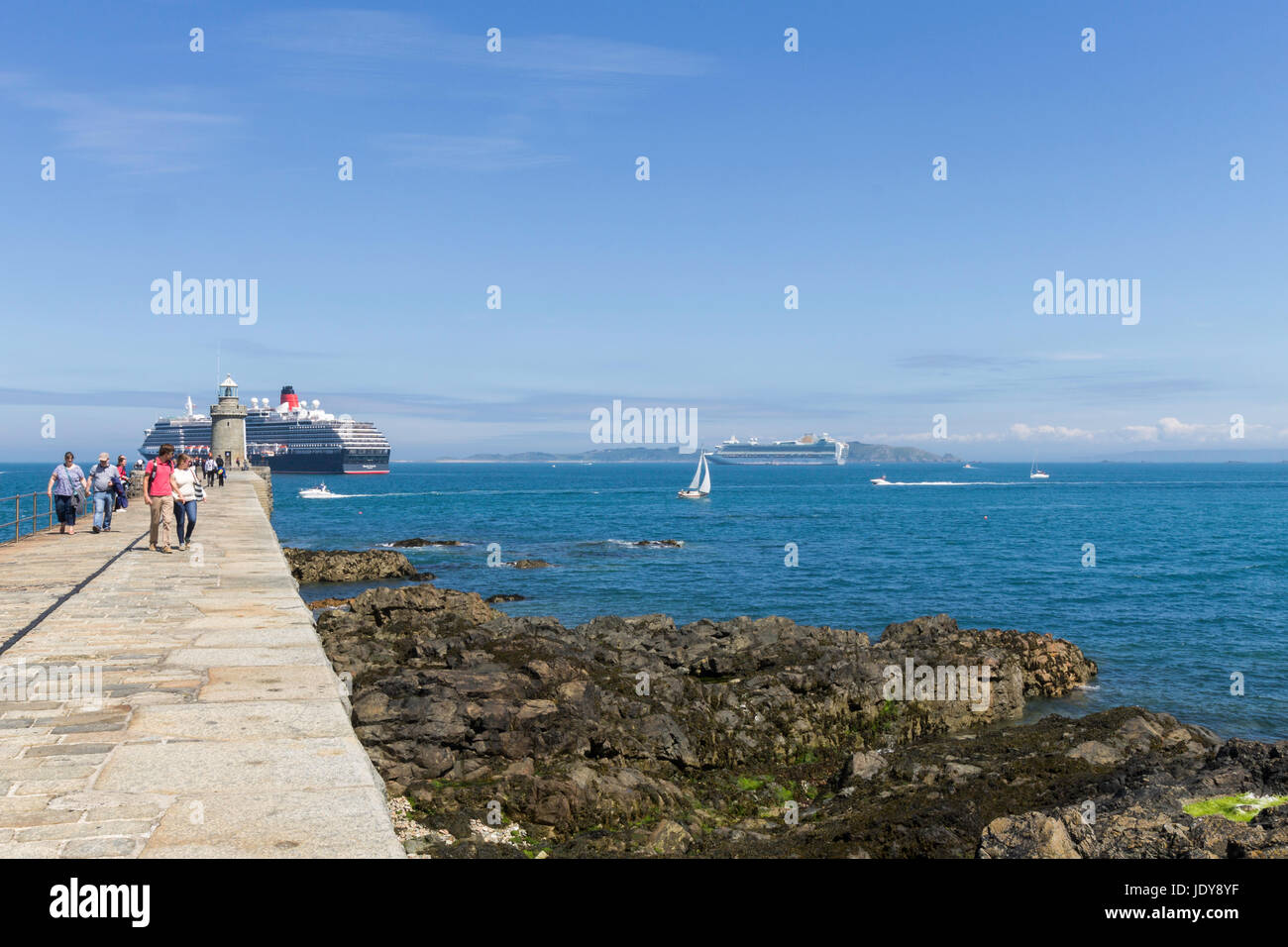 Touristen schlendern entlang Burg Wellenbrecher, Saint Peter Port, Guernsey. Ein Kreuzfahrtschiff ist Offshore verankert. Stockfoto