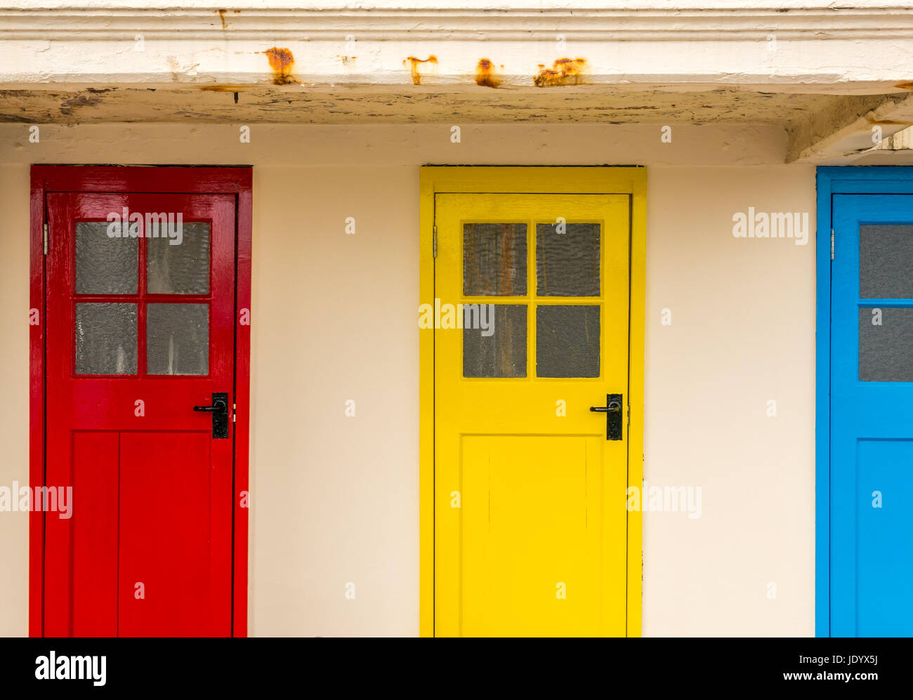 Reihe von bunten alten hölzernen ändern Schaltkastentüren in Grundfarben mit quadratischen Fensterscheiben North Berwick Hafen, East Lothian, Schottland, Großbritannien Stockfoto