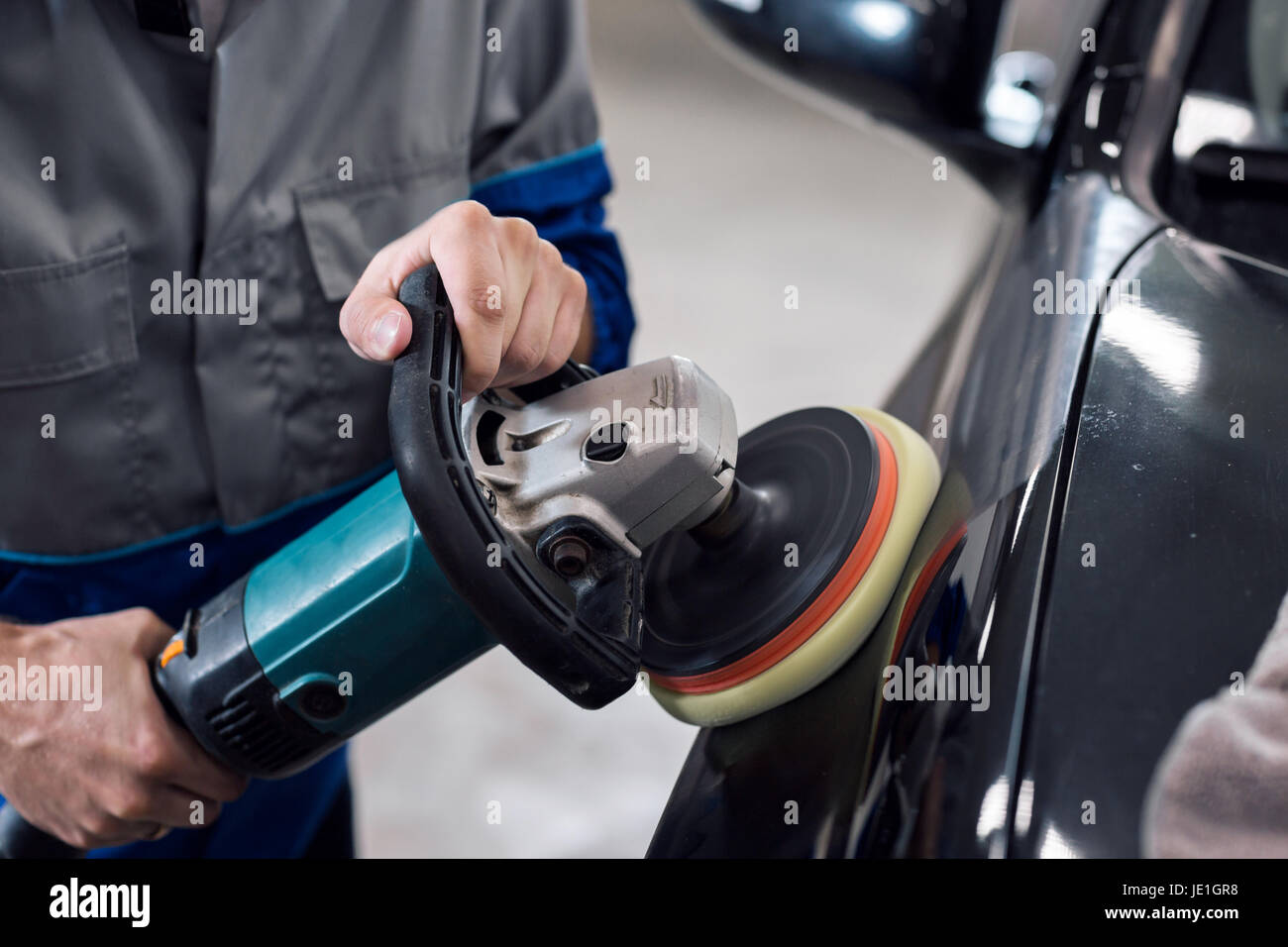 Nahaufnahme der Hände Arbeiter mit Schleifer, eine schwarze Karosserie in der Werkstatt zu polieren Stockfoto