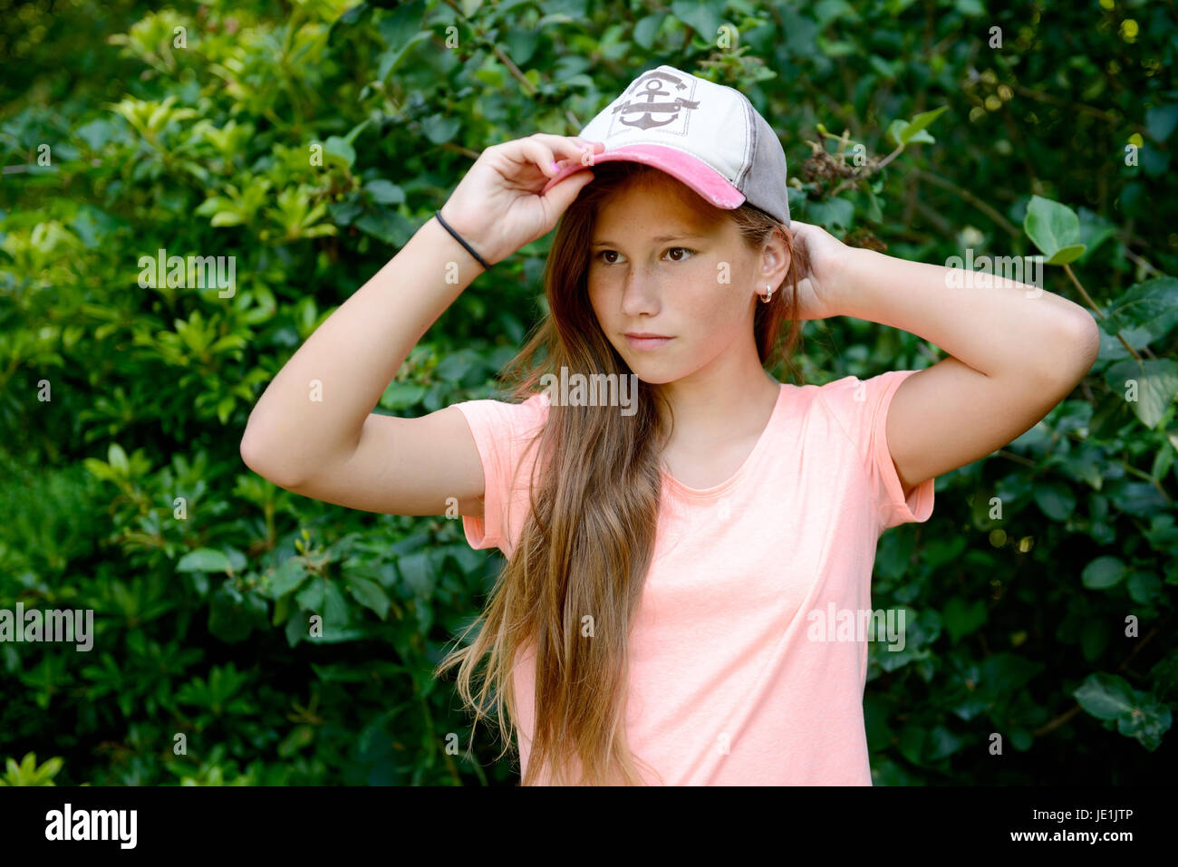Junge Teenager-Mädchen mit langen blonden Haaren mit Baseball-Kappe. Im Freien mit grünem Hintergrund. Stockfoto