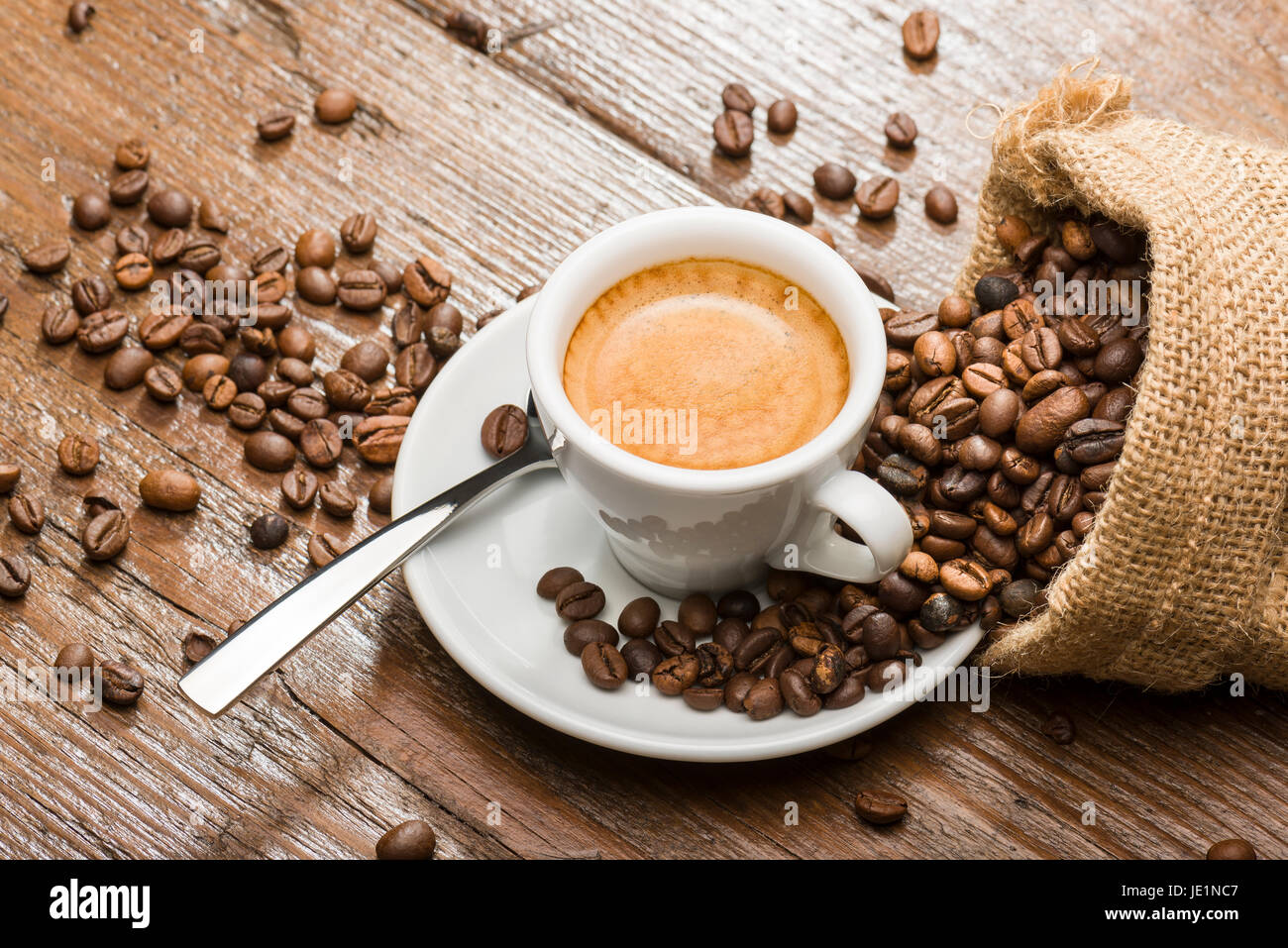 Tasse Kaffee mit Leinensack und Kaffeebohnen auf Holztisch. Stockfoto